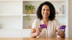 Mulher brasileira segurando um smartphone e um cartão roxo metálico parecido com o Nubank Ultravioleta, sorrindo enquanto pede o cartão